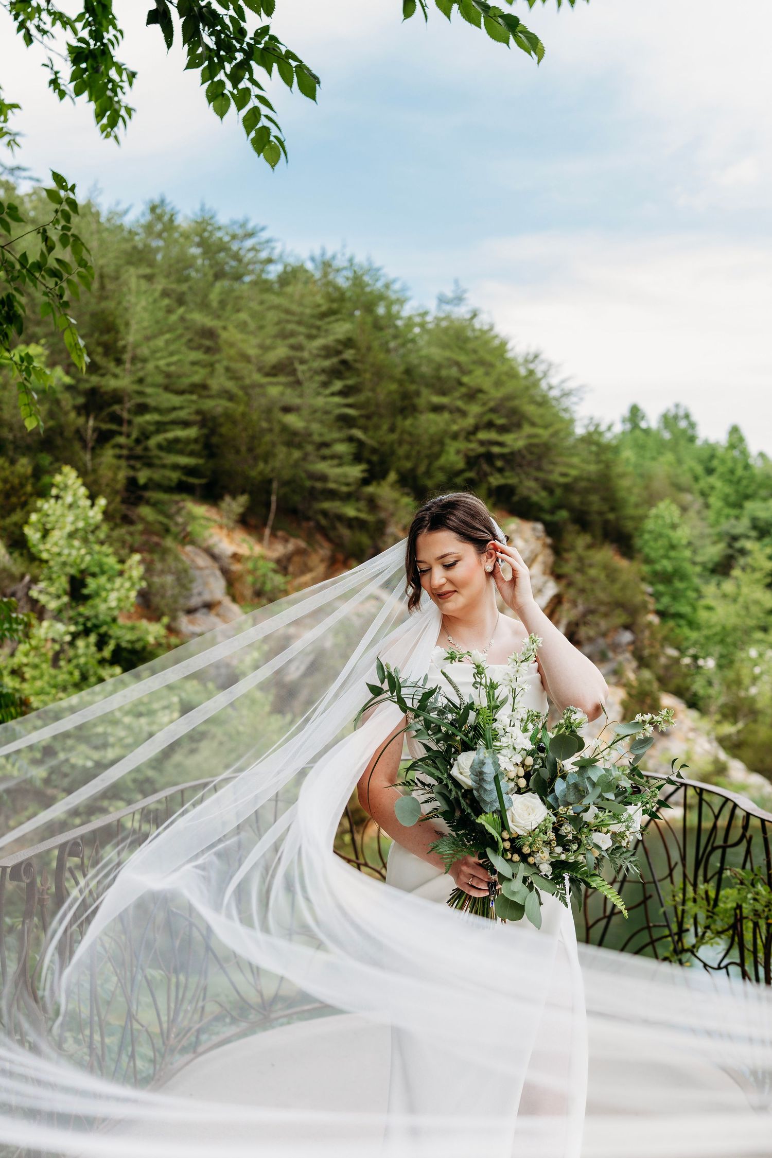 A radiant bride holds a white floral bouquet as her veil flows in the wind outdoors at Waterstone Venue in Johnson City, TN.