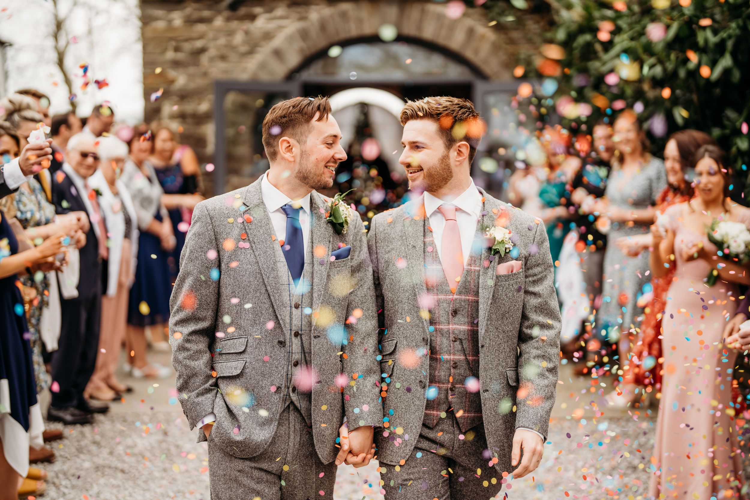 Wedding couple walking through confetti shower with guests celebrating in background.