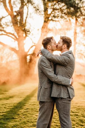 A romantic sunset moment between two people in matching grey suits embracing in a golden-lit park.
