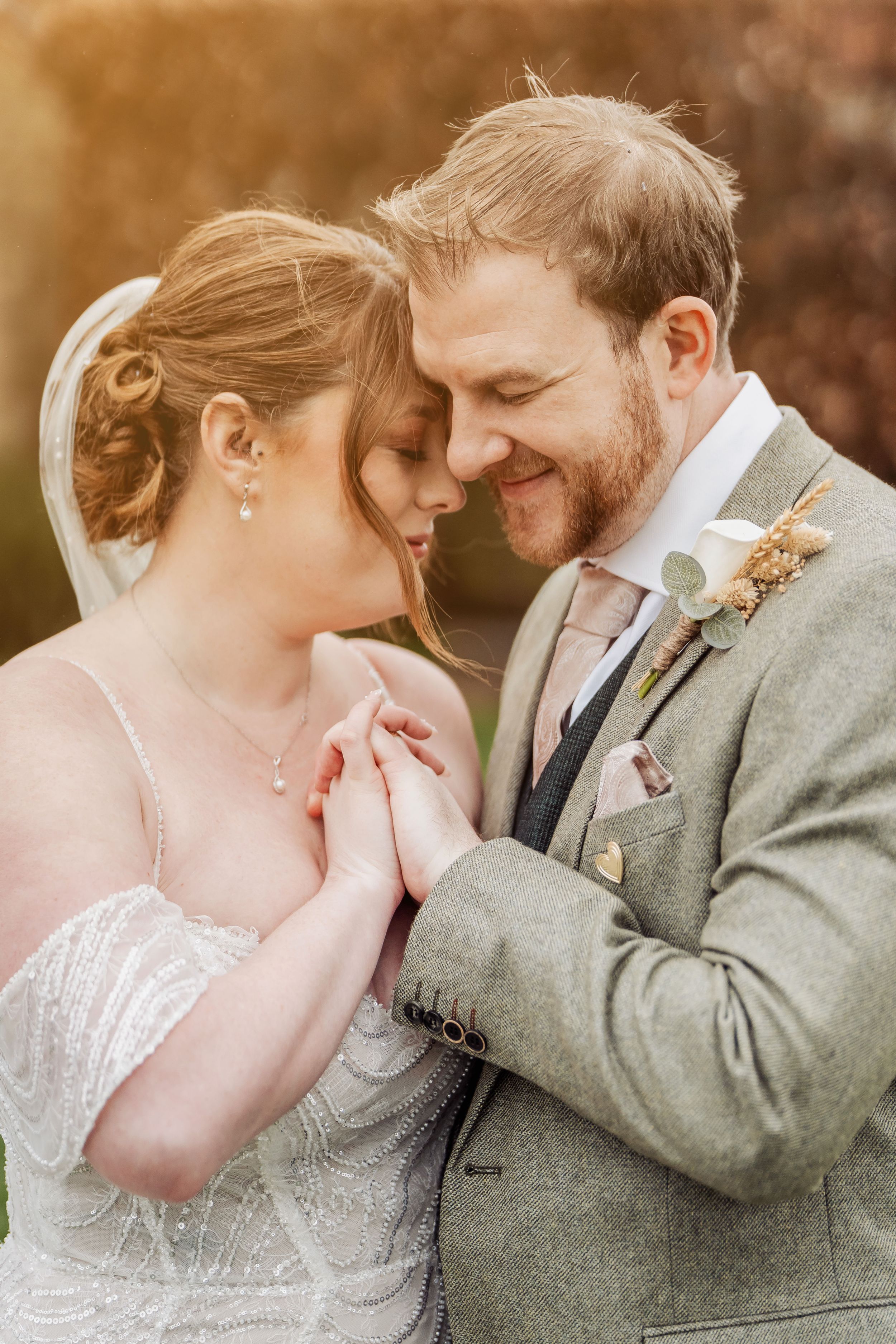 Intimate wedding portrait of couple in grey attire sharing tender moment at sunset.
