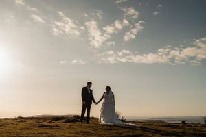 Silhouetted couple holding hands against sunset sky on coastal cliff.