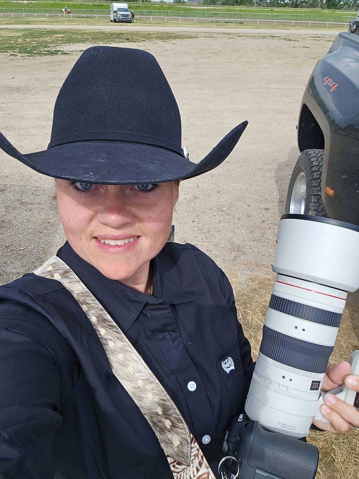 A photographer in western attire displays professional camera equipment outdoors.