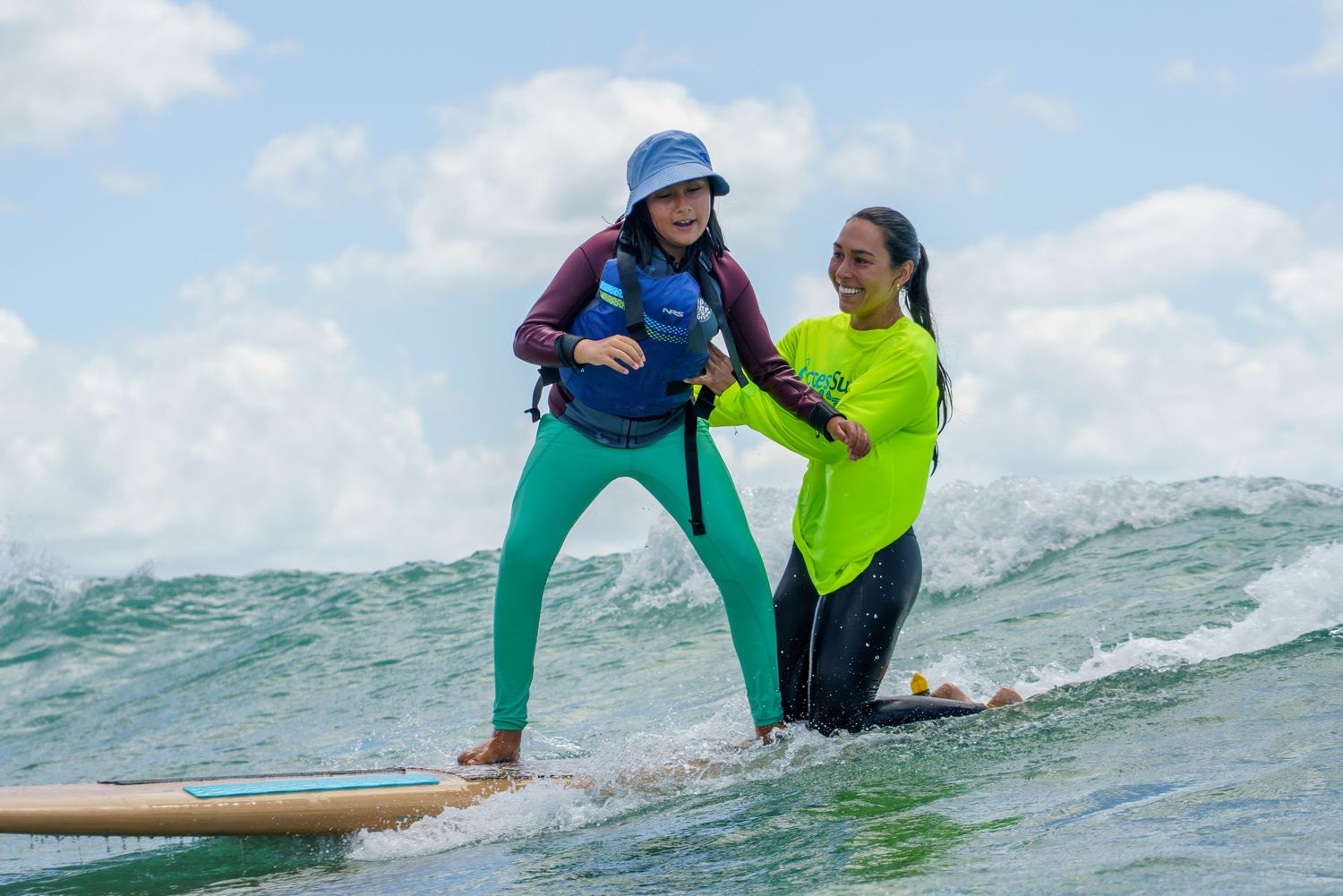 Surf instructor, Maddie, teaching student to balance on surfboard in rolling ocean waves.