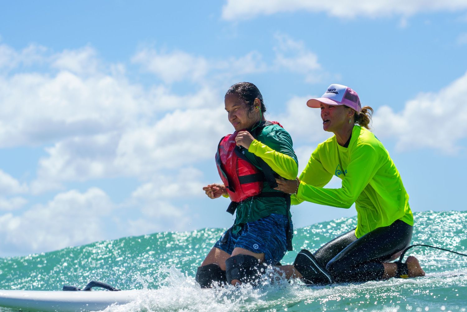 Two people practicing surfing techniques on board in turquoise ocean waves.