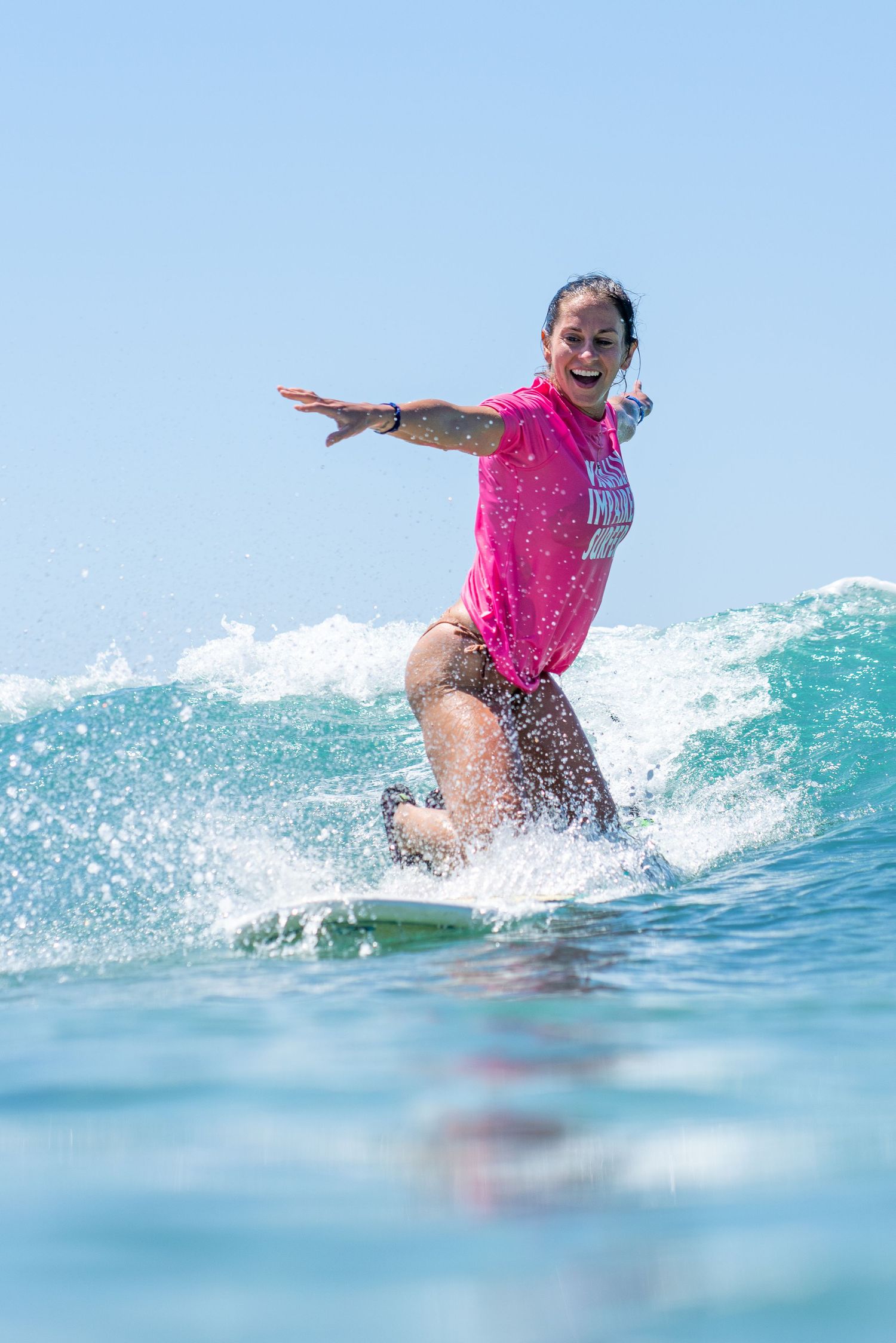 Surfer in bright pink shirt riding a wave while maintaining perfect balance.