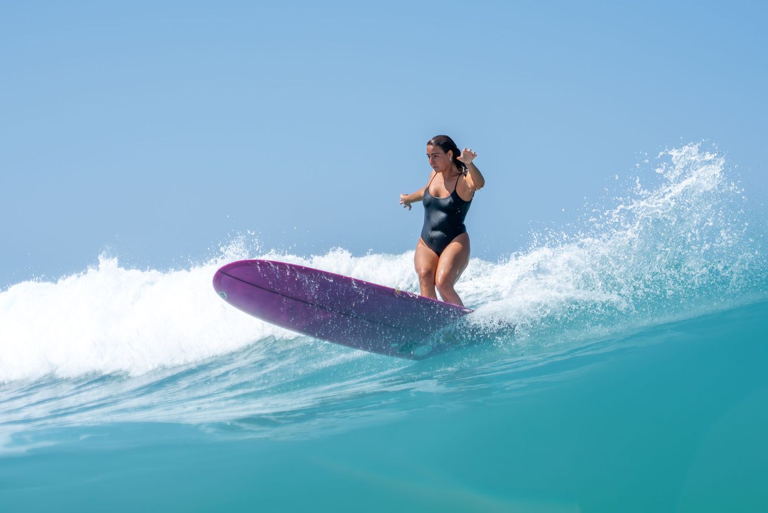 Surfer riding purple surfboard on turquoise wave in tropical waters.