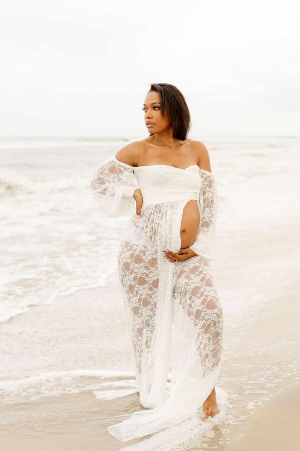 White lace sheer dress flows elegantly as someone poses gracefully at a sandy beach during sunset.