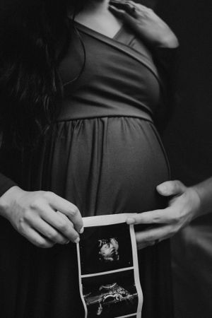 Black and white photo of pregnant woman holding ultrasound images.