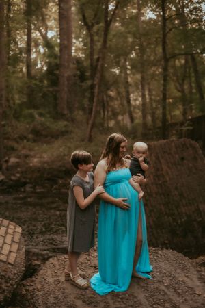Expectant mother in turquoise dress with children in forest setting.