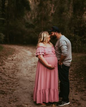 Expectant couple in romantic pose on forest path at sunset.