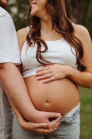 Close-up maternity photo showing hands cradling a pregnant belly in natural outdoor lighting.