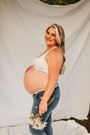 Maternity photoshoot against white backdrop showing pregnant woman in jeans and crop top.