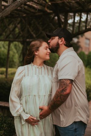An intimate maternity photo showing a couple embracing under tree branches at sunset.