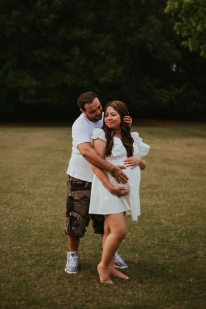 A couple shares an intimate moment outdoors during their maternity photoshoot.