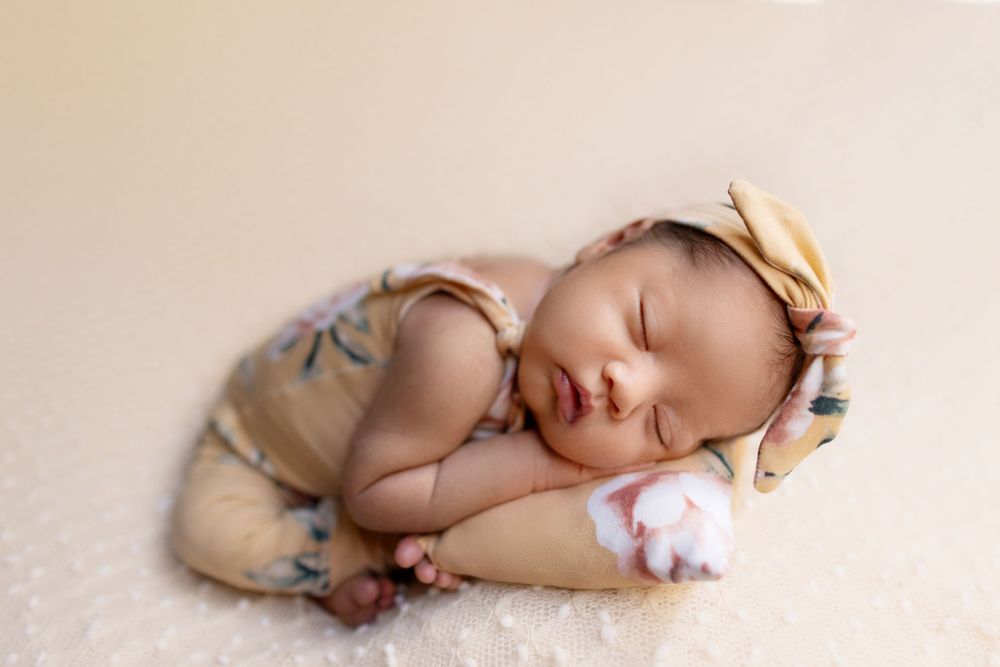 Sleeping newborn baby wrapped in cream tones on neutral background.