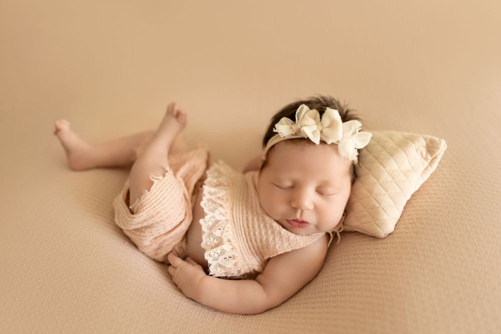 Sleeping newborn in cream knit wrap on beige background.