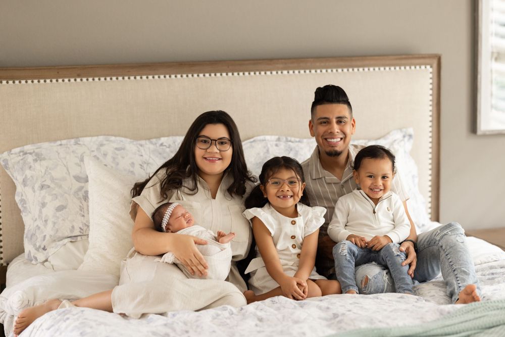 Family lounging together on white bedding for casual indoor portrait.