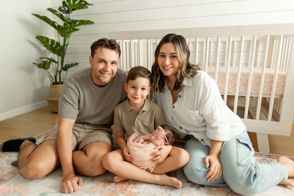 Relaxed family portrait on bed with white linens and green plant decor.