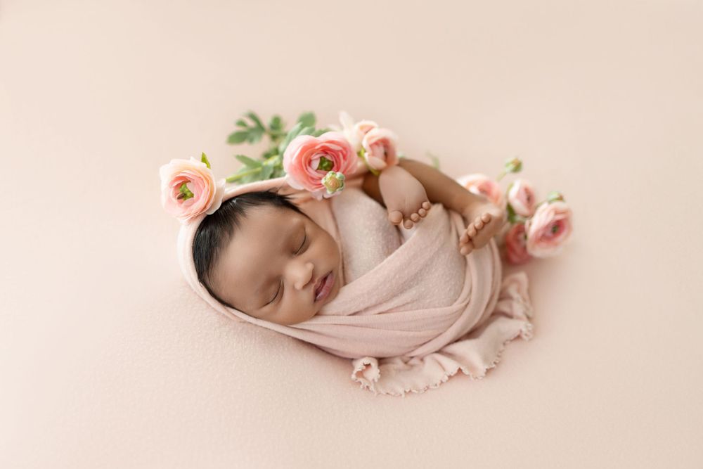 Newborn baby in pink outfit sleeping peacefully on beige background with soft pink floral accents.
