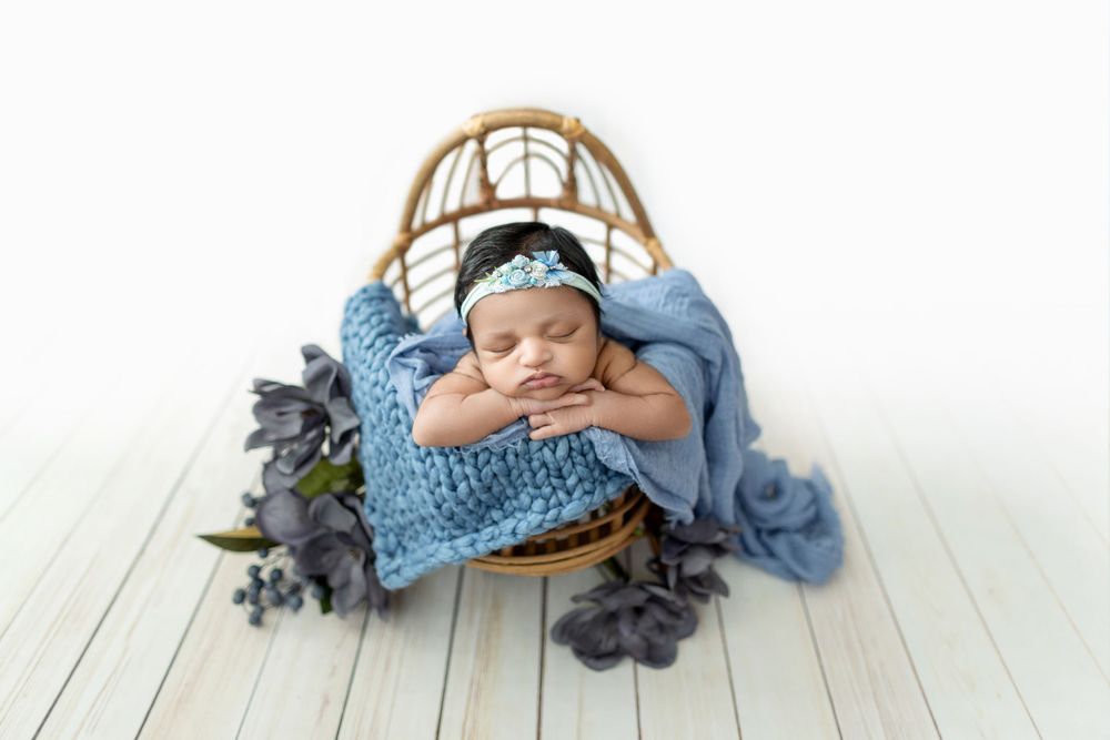 Sleeping newborn in blue outfit lying on white wooden floor with decorative basket.