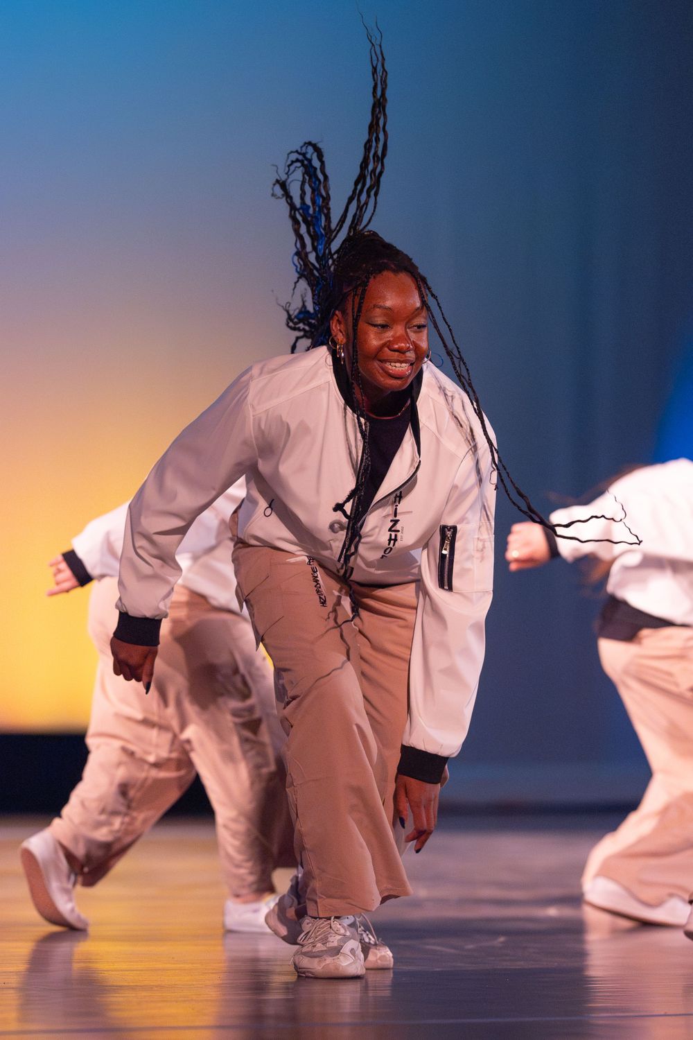 Dancer in white jacket and khaki pants performs energetic hip hop moves on stage.