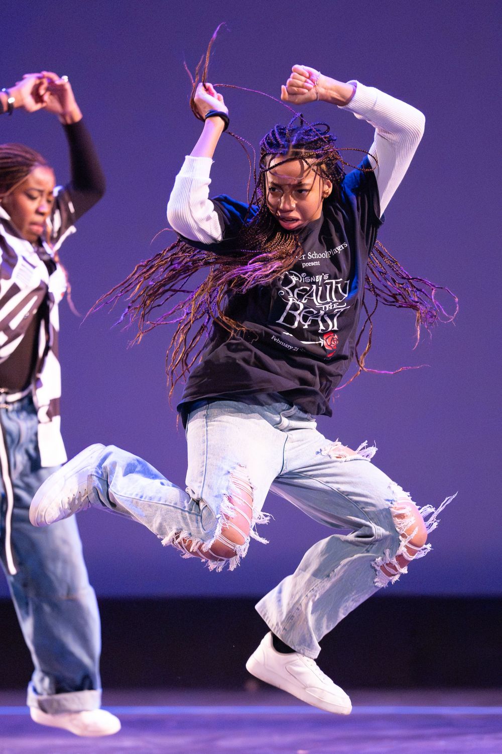 Dancers perform dynamic hip hop moves in casual streetwear on purple-lit stage.
