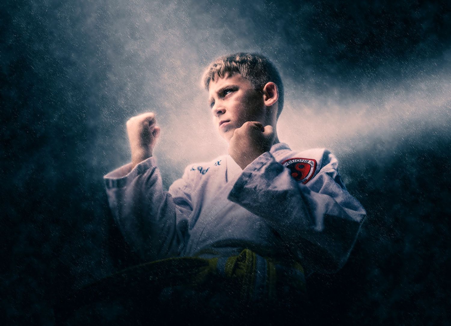 Karate student in white uniform posed against dark background with atmospheric lighting.