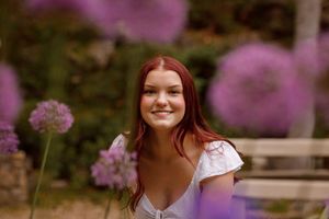 Purple wildflowers bloom in a garden while a person in a white top poses among the natural scenery.