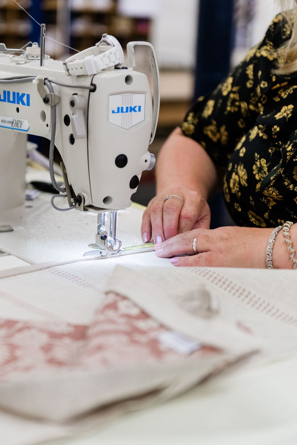 Close-up view of hands operating a Juki industrial sewing machine with fabric material on the work surface.