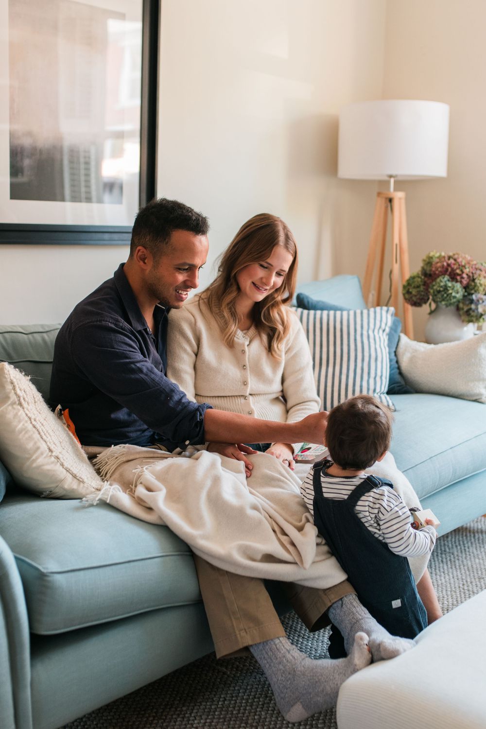 Family relaxes together on light blue couch in bright modern living room with playful interactions.