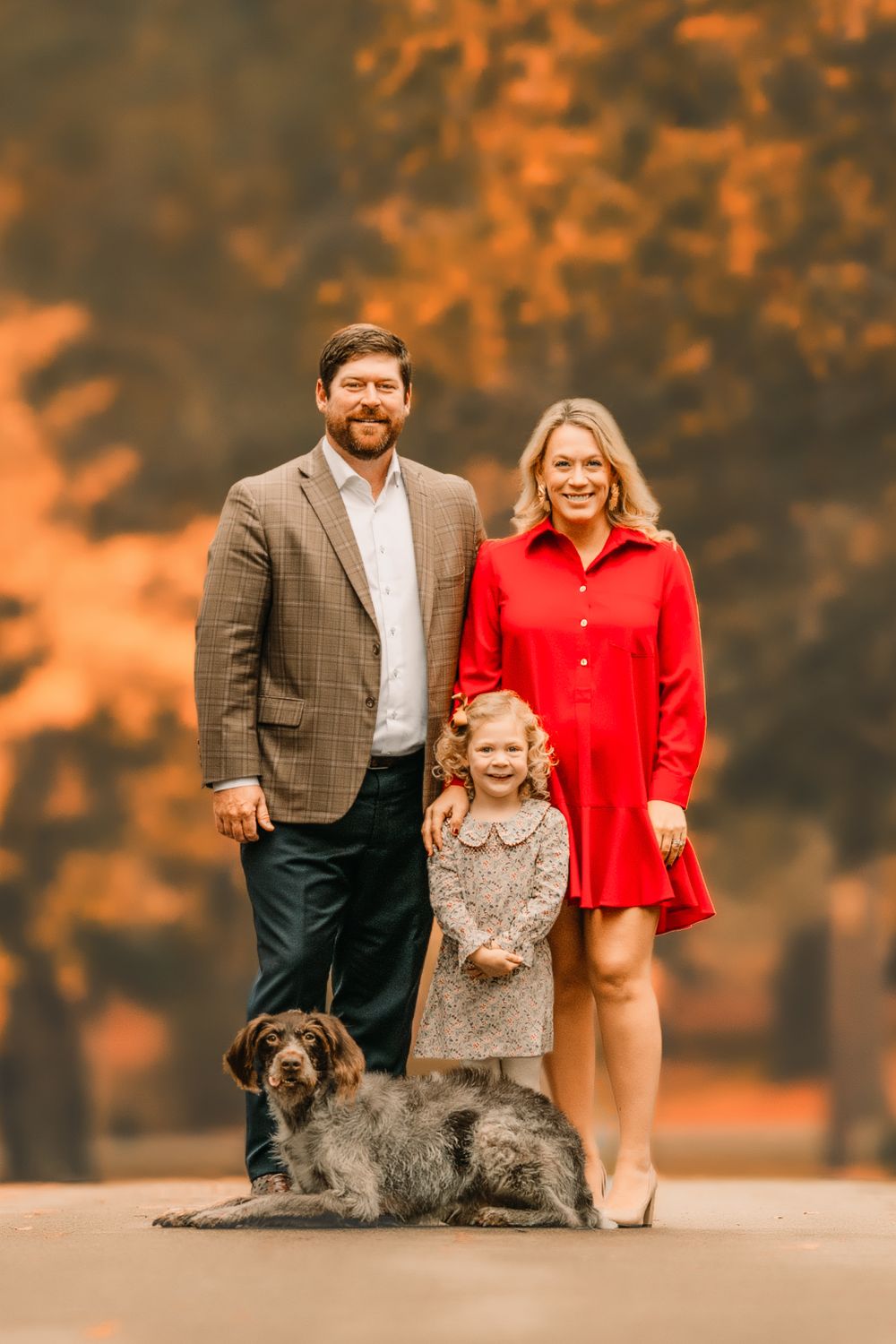 A sweet family photo outdoors with a beloved dog amid golden fall foliage.