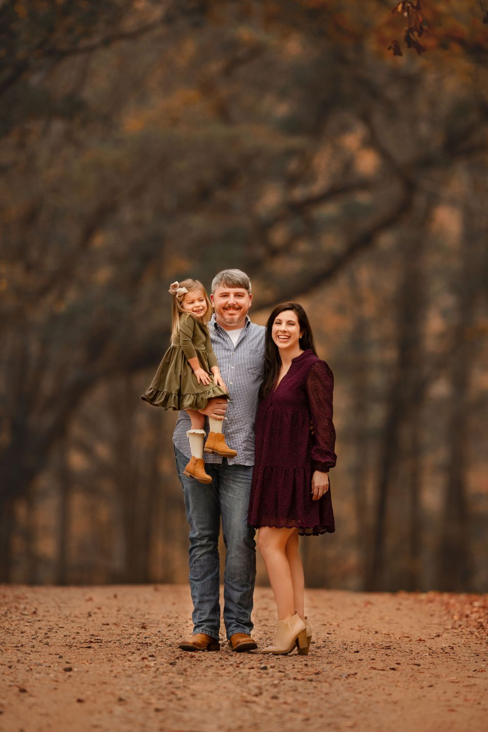 A couple poses together on a path covered in fallen autumn leaves.