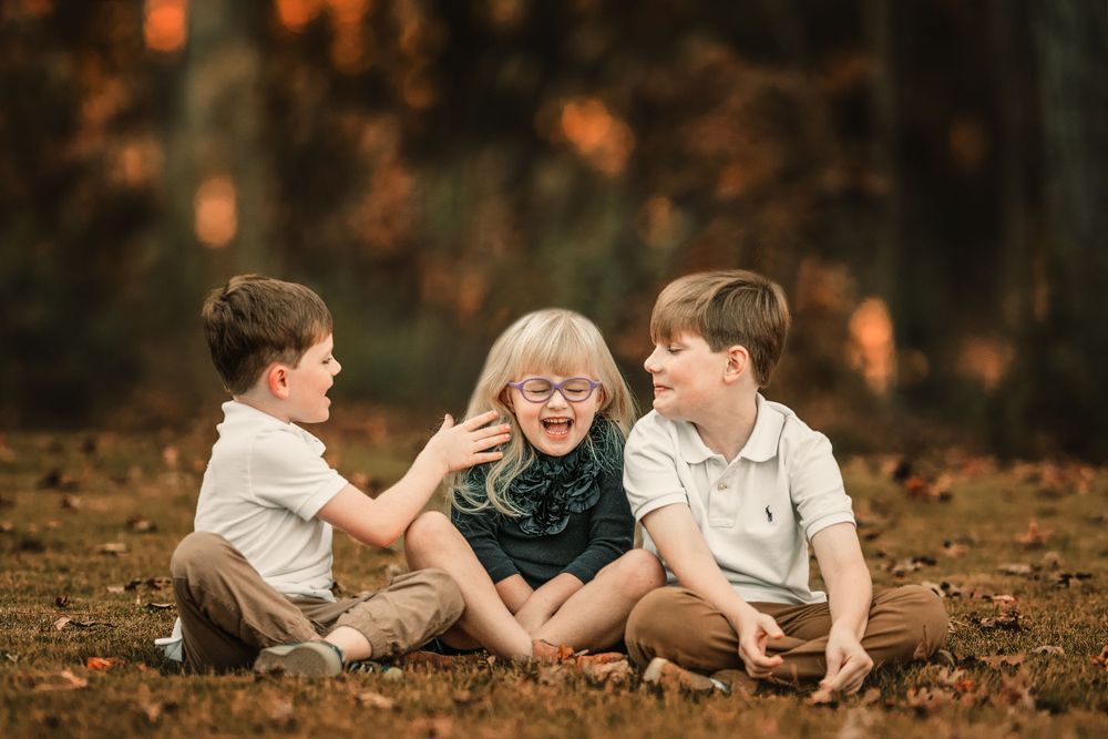 Children play and laugh together on autumn ground with warm orange lighting.