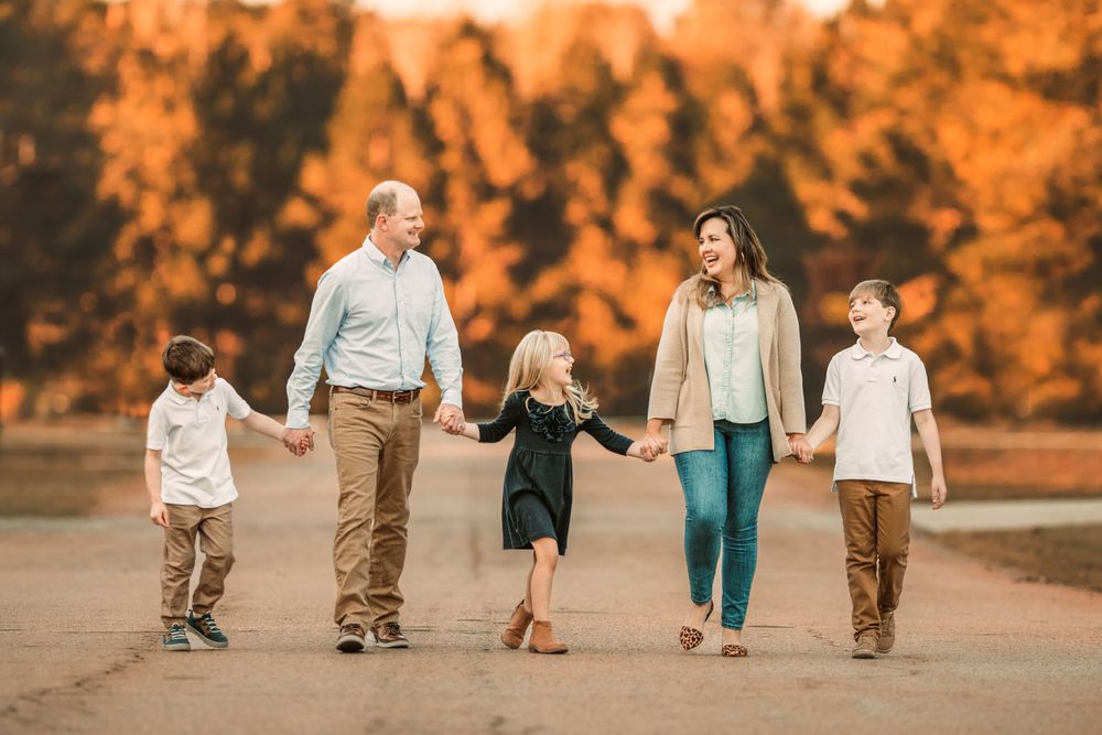 Group of children walking hand in hand through fall foliage with golden sunset lighting.