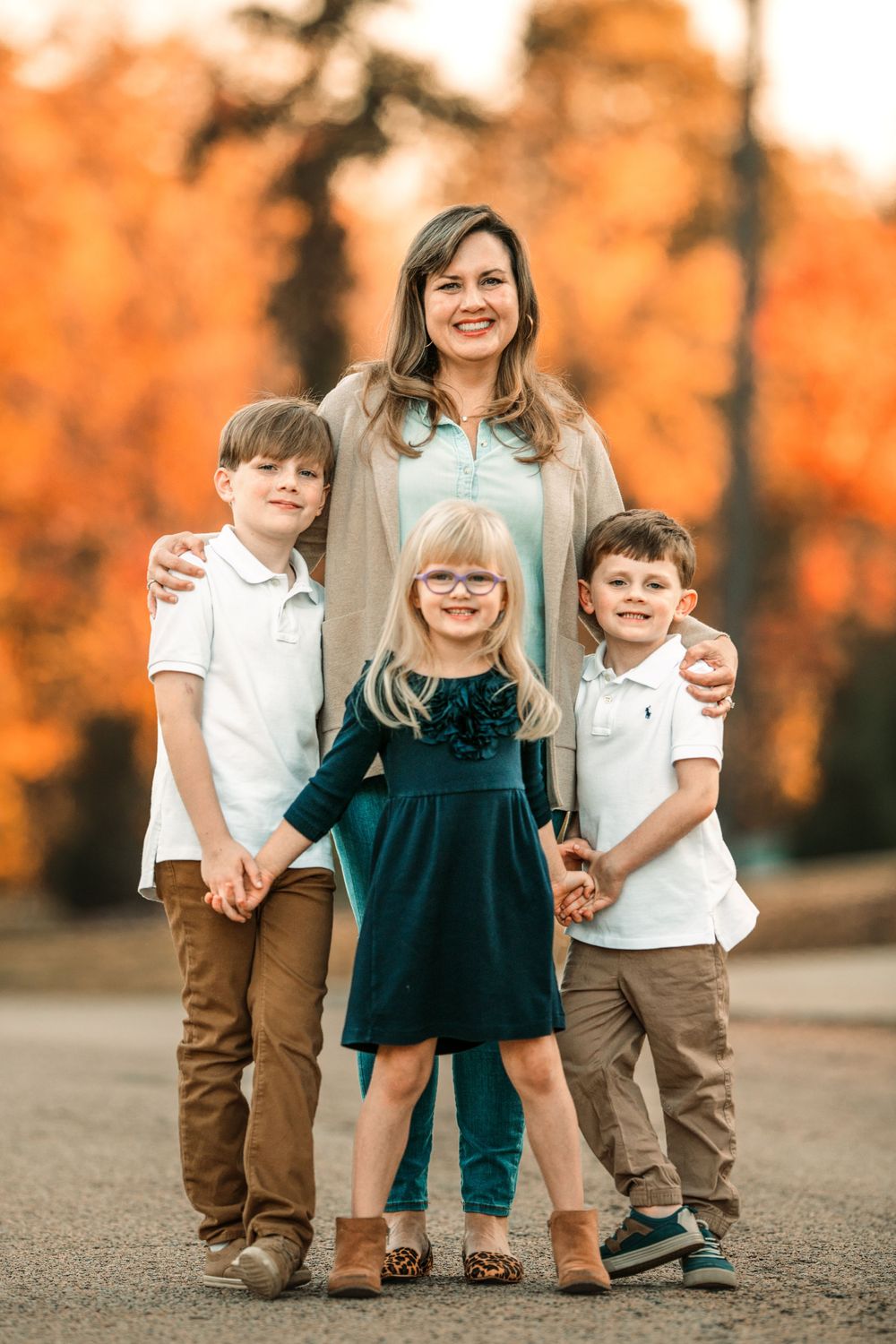 Family group poses together outdoors during golden hour with autumn colors in background.