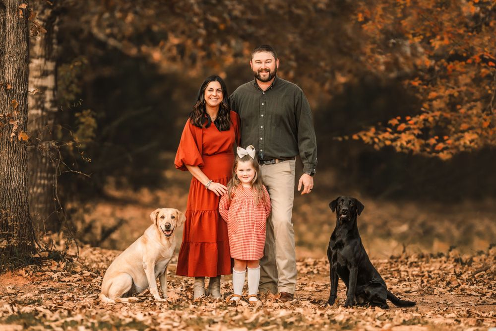 A family and their two dogs pose together on a leaf-covered path in autumn.