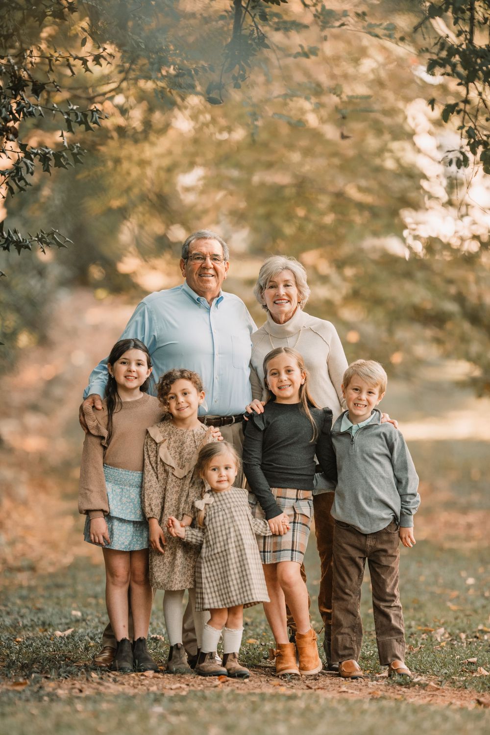 A multi-generational family poses together outdoors during autumn with warm golden lighting in nature.