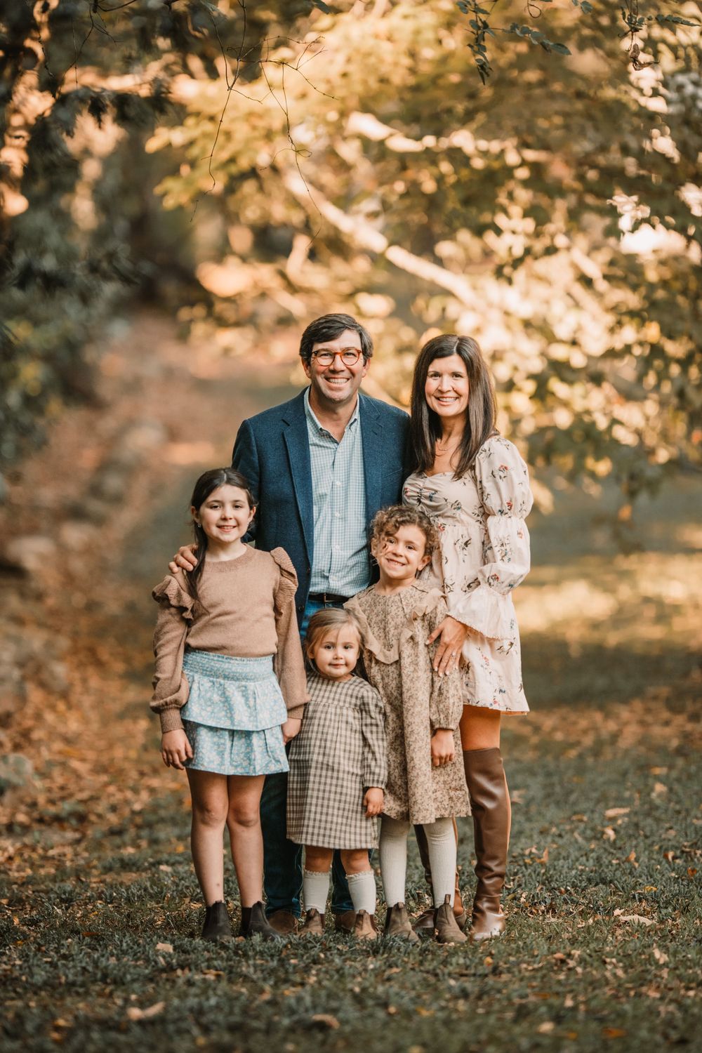 A family stands together outdoors in autumn with falling leaves and warm golden lighting creating a cozy atmosphere.