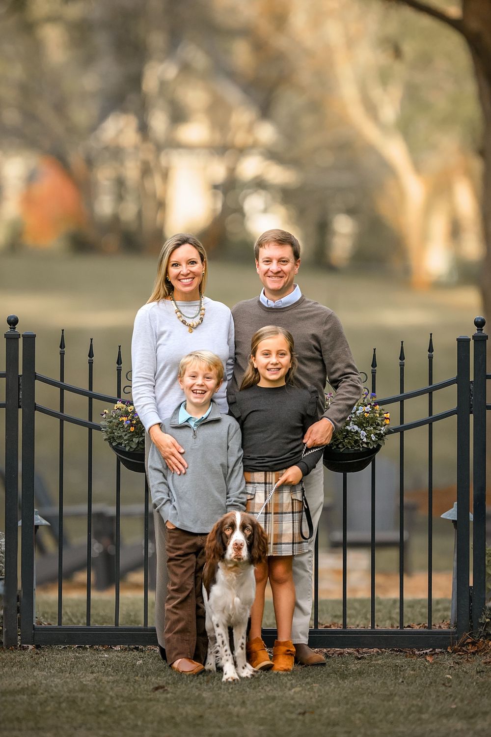 Family and their brown and white dog pose together near an iron gate in an outdoor autumn setting.