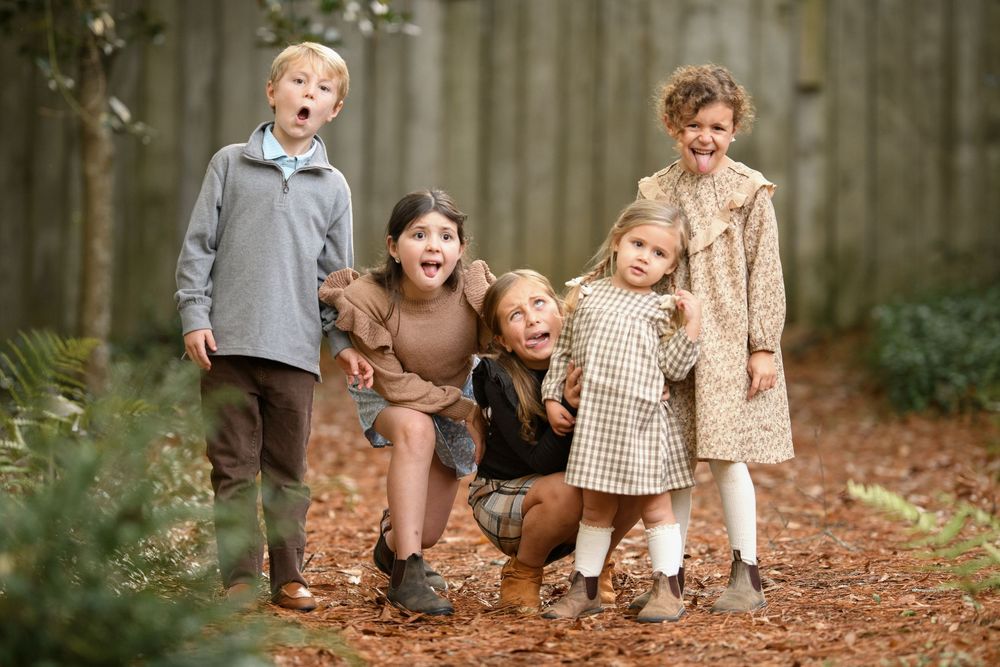 Family in casual fall outfits laughs and plays together during an autumn outdoor photo session in a wooded area.