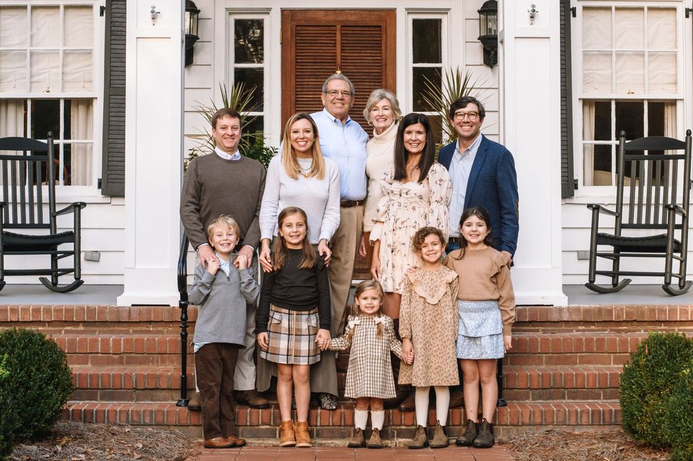 Multi-generational family portrait on white colonial house steps.