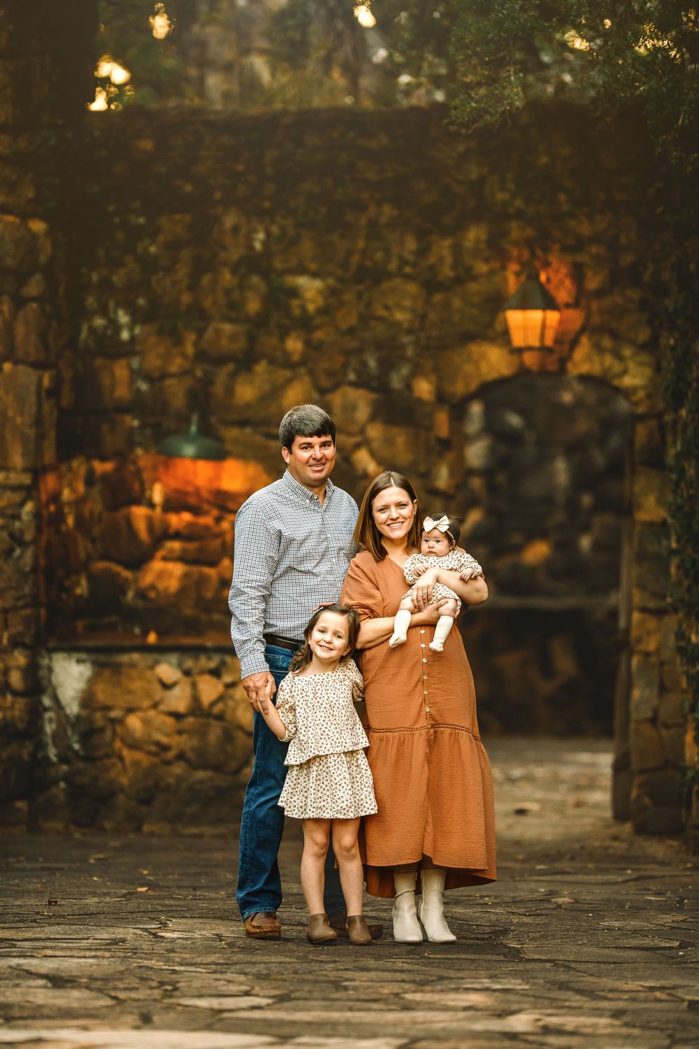 A family portrait taken against a rustic stone wall with warm autumn lighting.