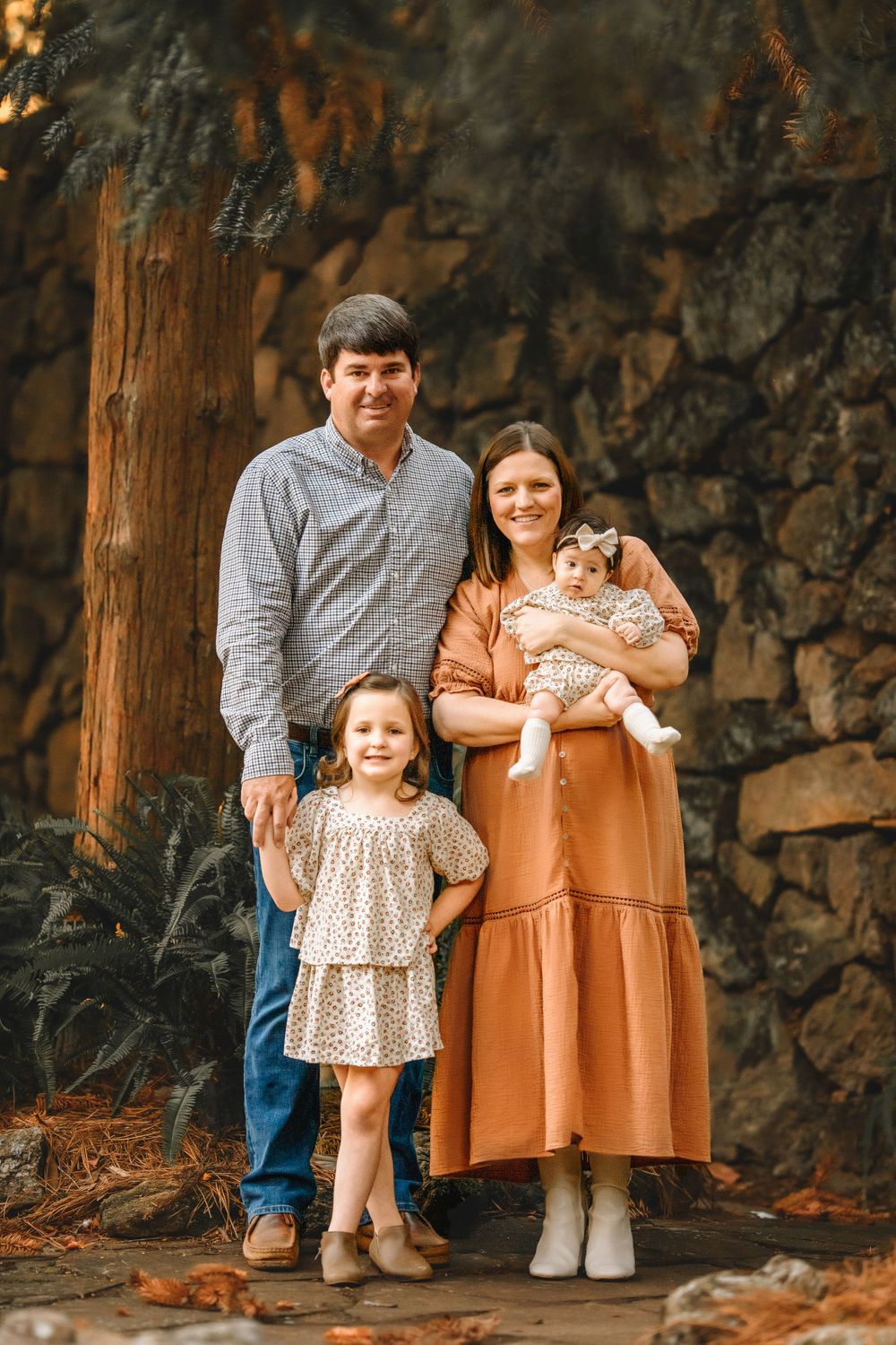 A casual family portrait against a stone wall backdrop in coordinated earth-tone outfits.