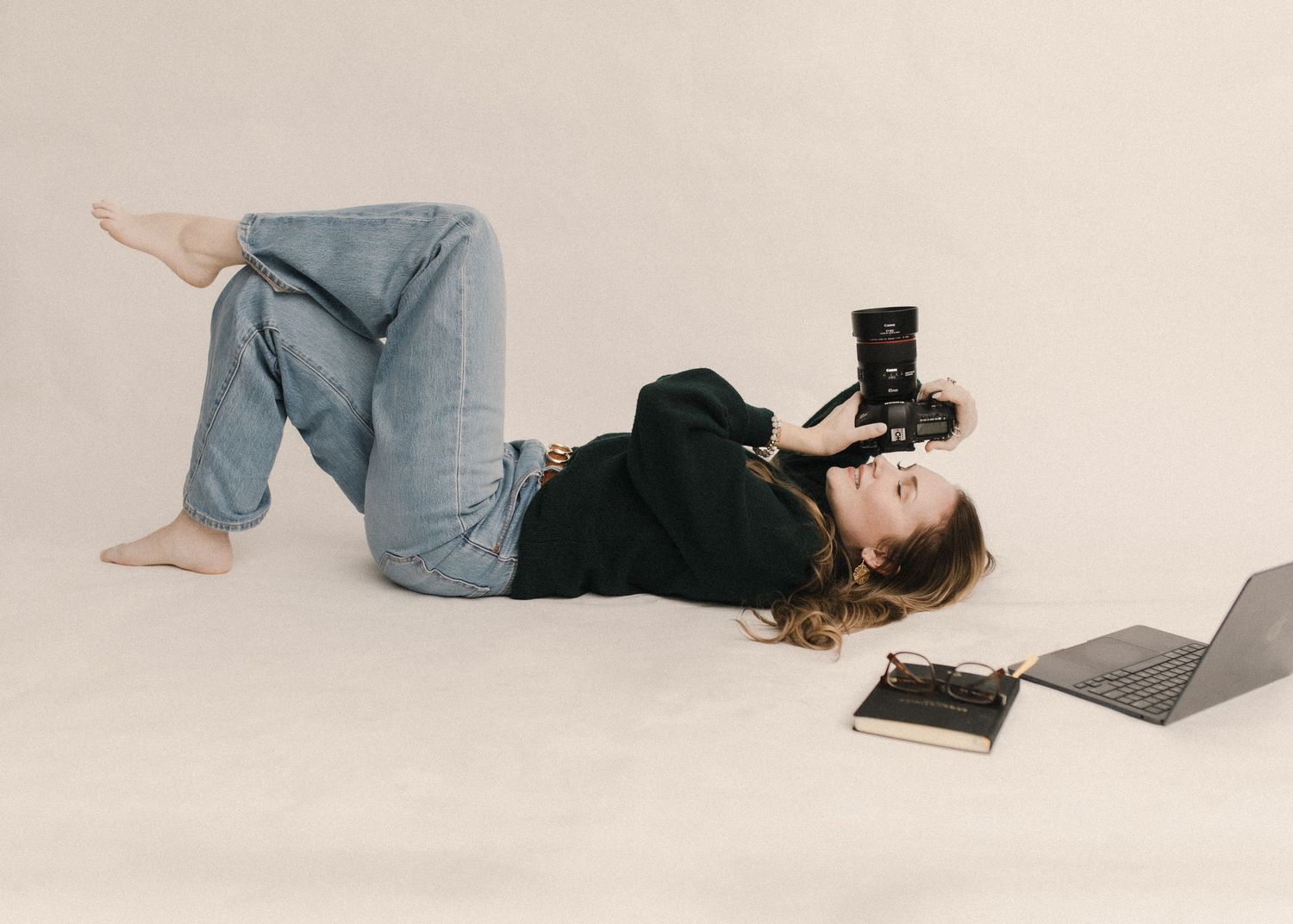 Heather Cahoon lying on floor in casual wear with jeans and sweater, using camera with laptop and book nearby.
