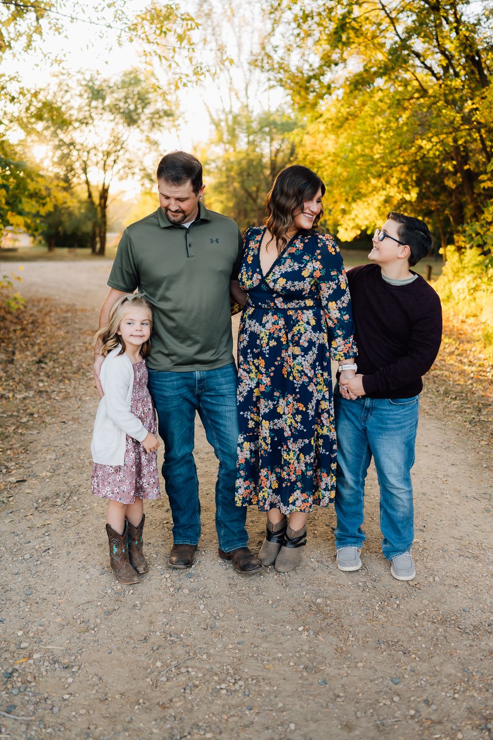 Family of four walking together on a dirt path surrounded by golden autumn trees.