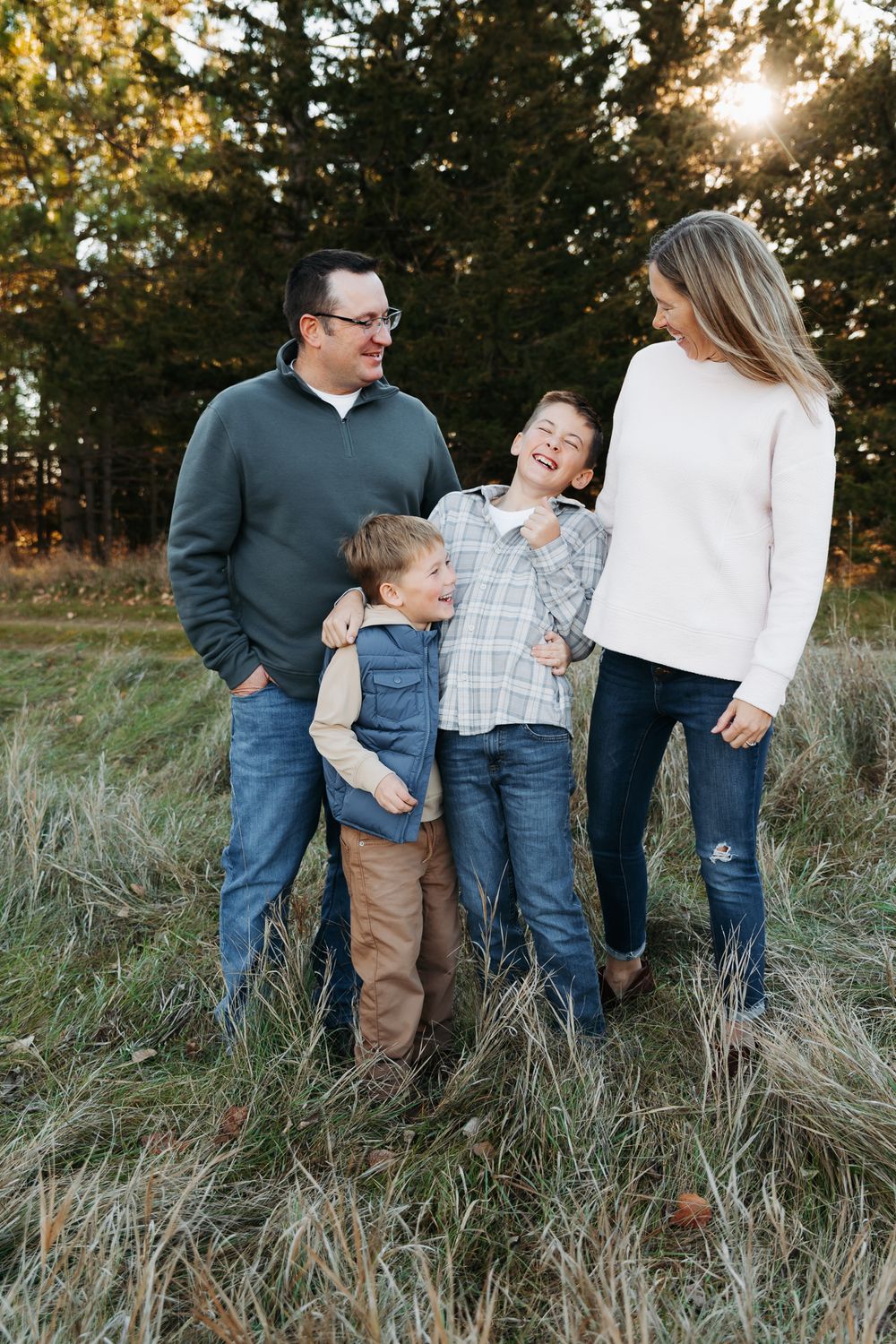 A family wearing coordinated blue and white outfits shares candid moments together in a grassy field at sunset.