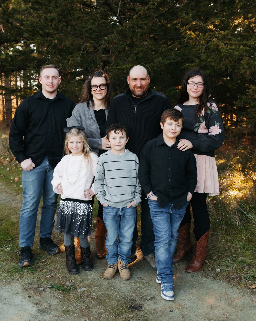 A group poses together outdoors during an autumn family photoshoot with trees in the background.