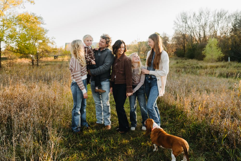 Family group poses together in a scenic autumn field during golden hour sunset photography session.