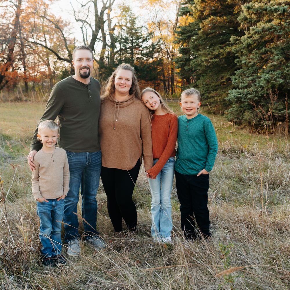 A group stands together in tall autumn grass during a casual outdoor photo session at sunset.