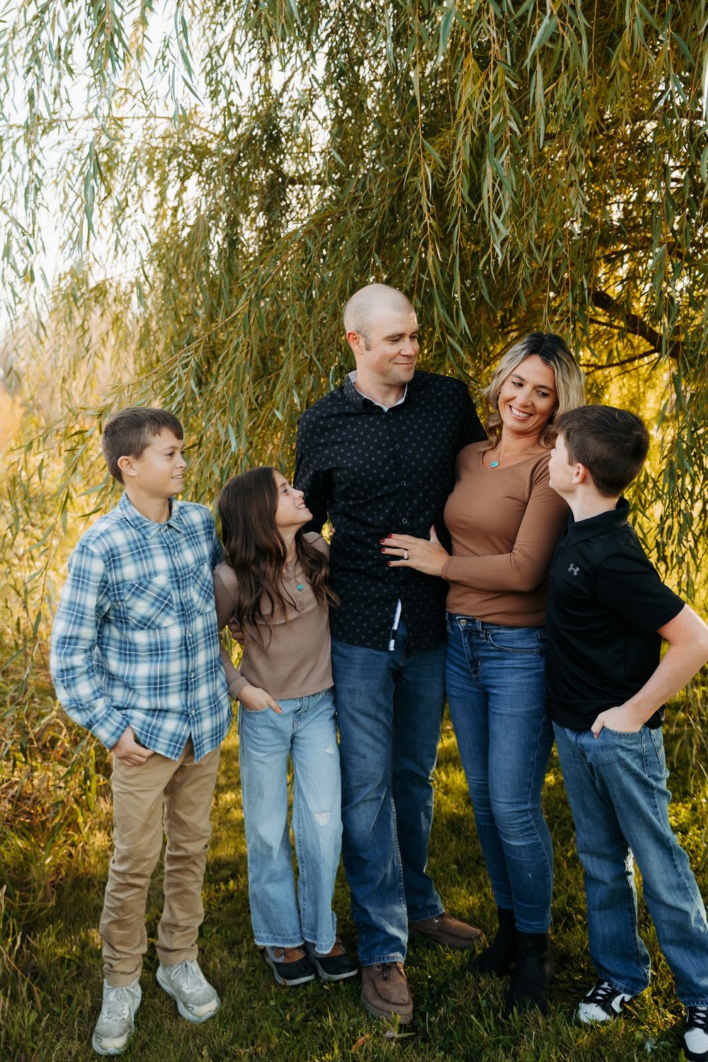 A group poses together under a weeping willow tree during a casual outdoor photo session.